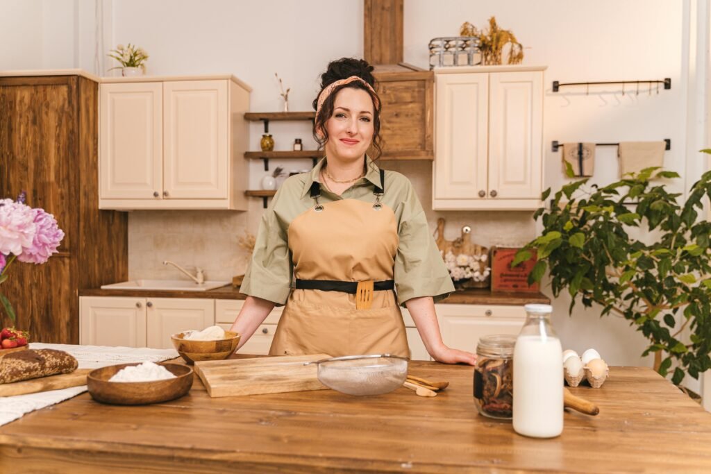 Smiling woman in apron preparing food in a cozy rustic kitchen setting.